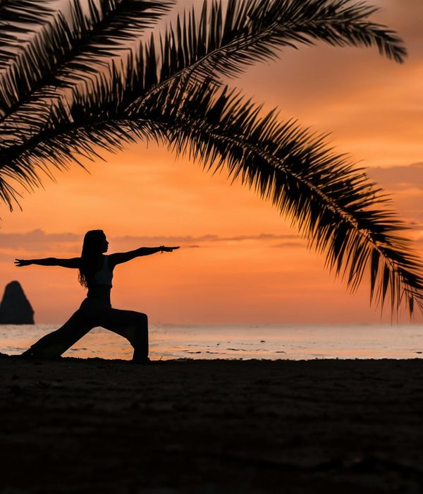 Smiling woman doing a strong warrior yoga pose on a tropical beach at sunrise.